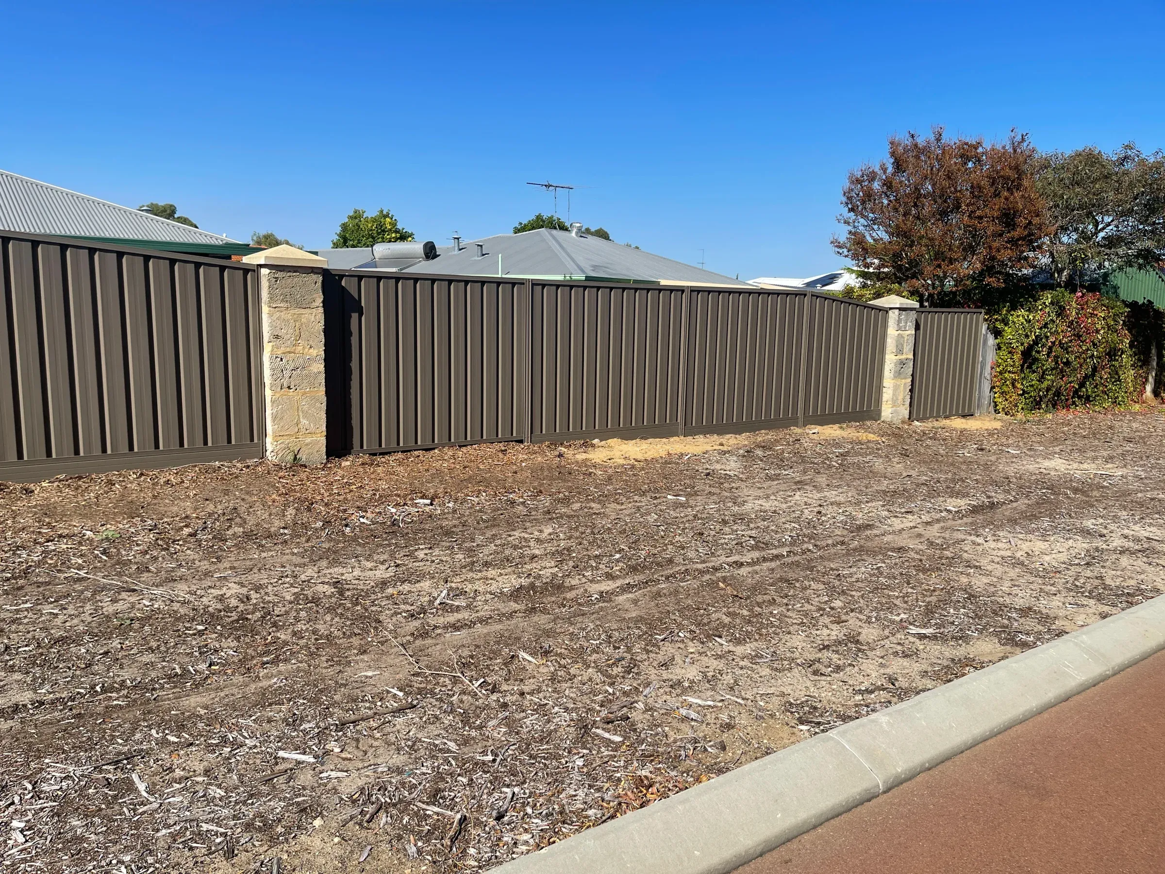 Dark Colorbond front boundary fence with limestone piers on a levelled block