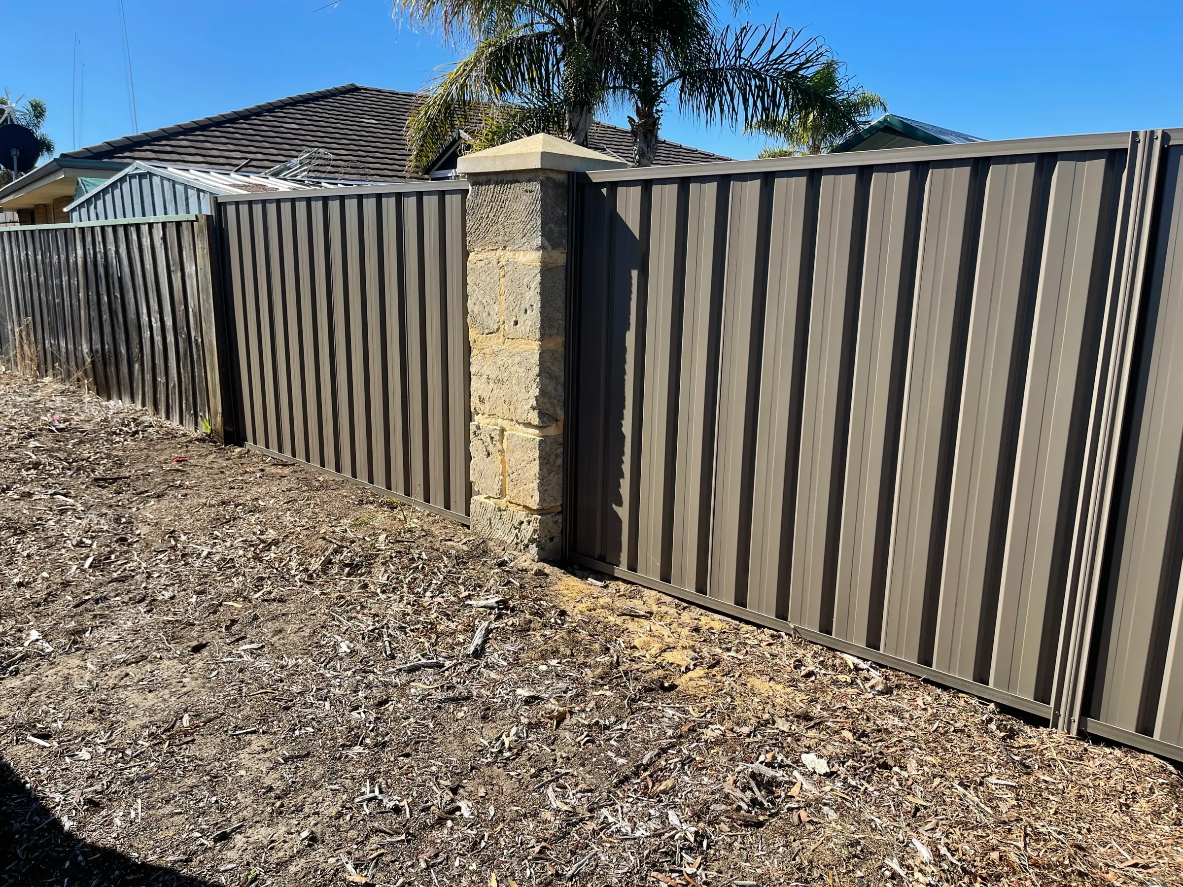 Dark Colorbond fence meeting a limestone pier at the corner of a front boundary