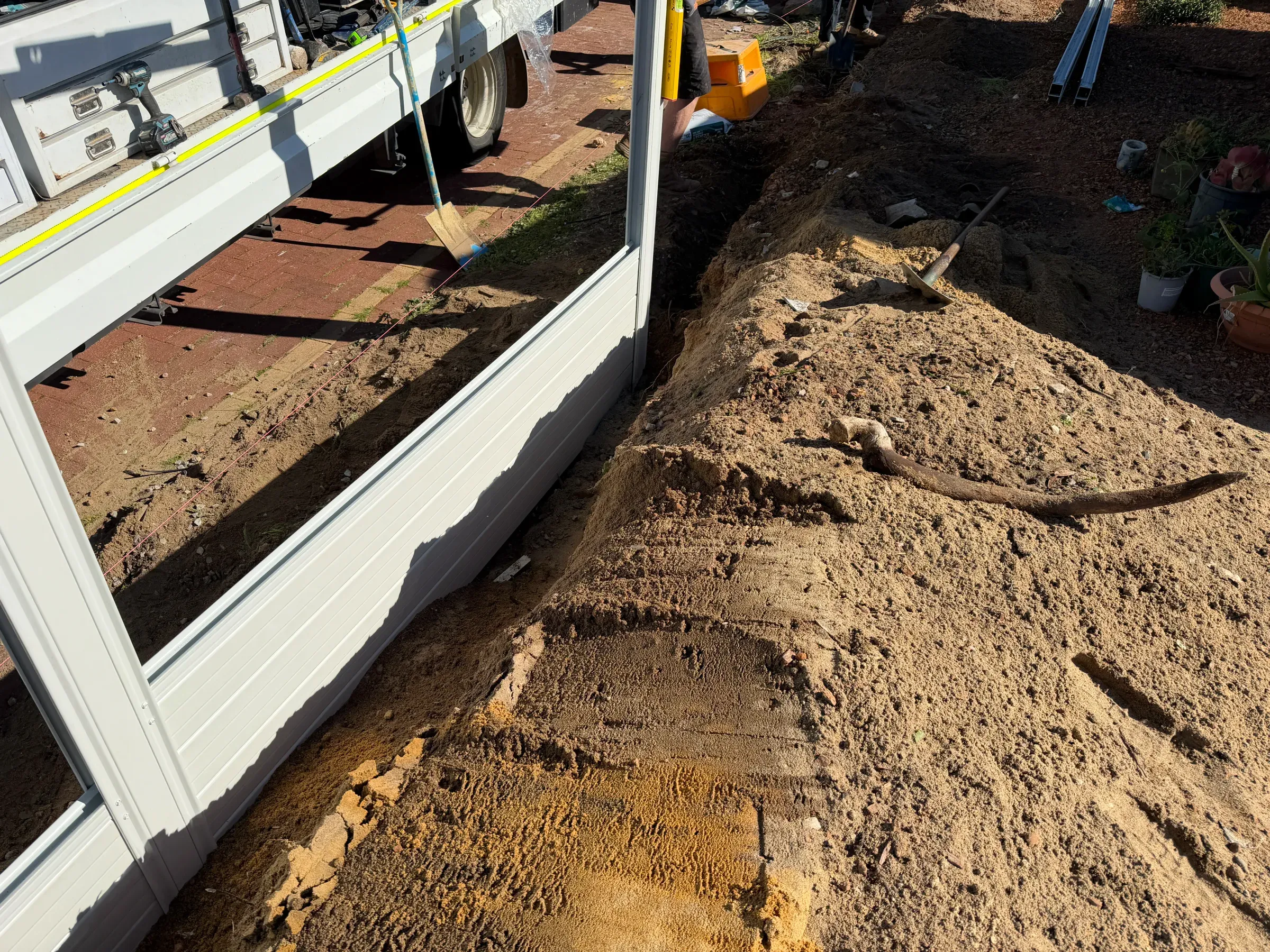 Fence panels stacked beside an open footing trench with the excavator spoil still on the ground