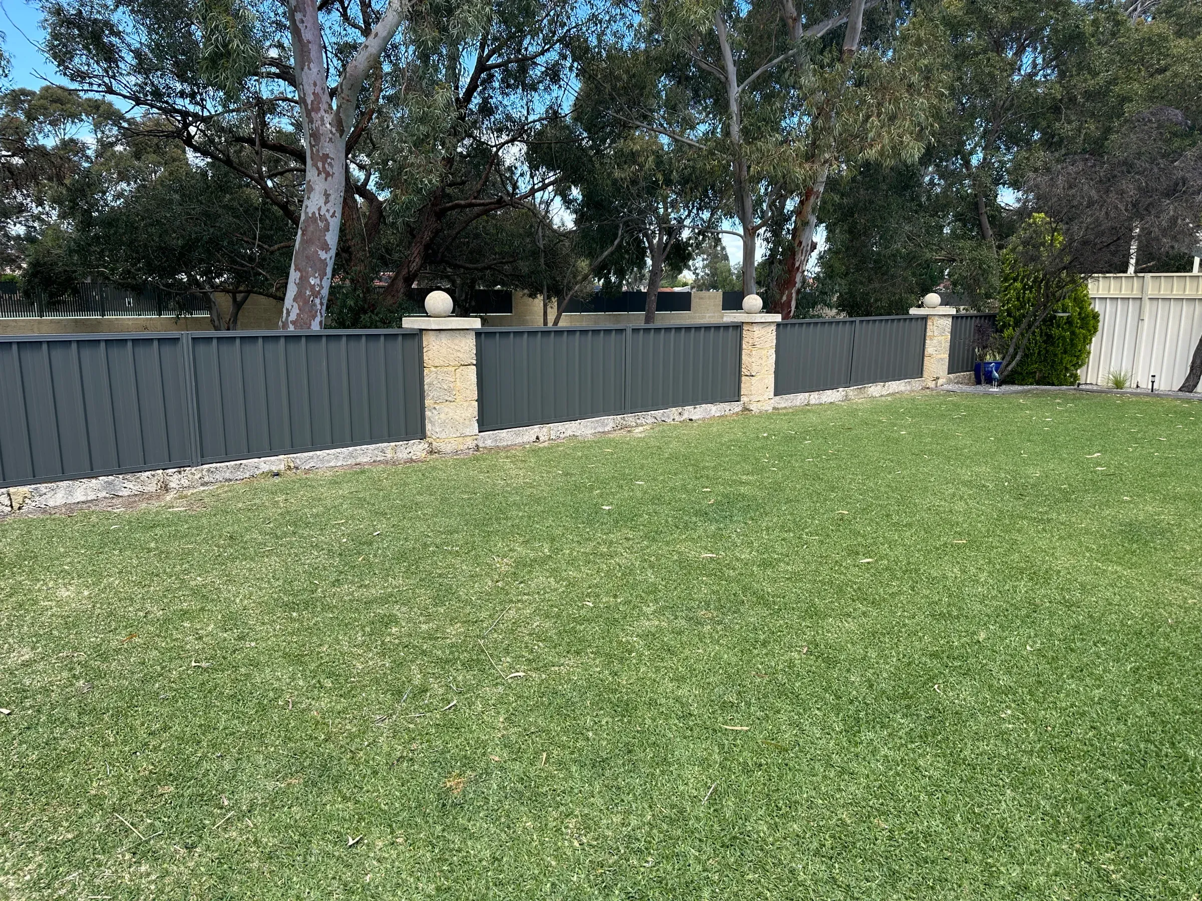 Green Colorbond infill panels between rendered limestone piers, seen across a front lawn