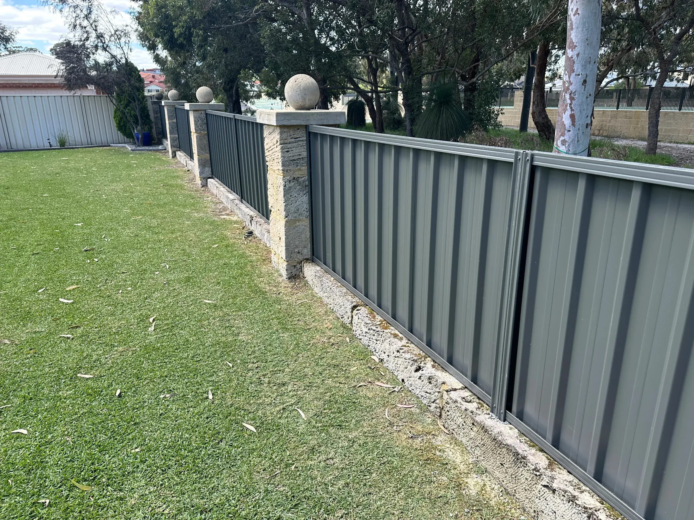 Green Colorbond fence with limestone piers stepping down a sloping front boundary