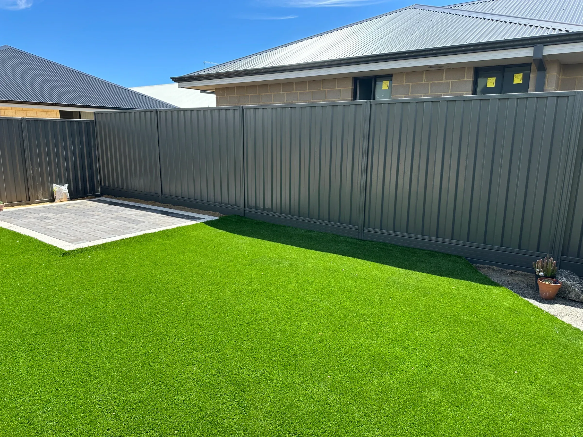 Grey Colorbond boundary fence along a courtyard laid to synthetic turf