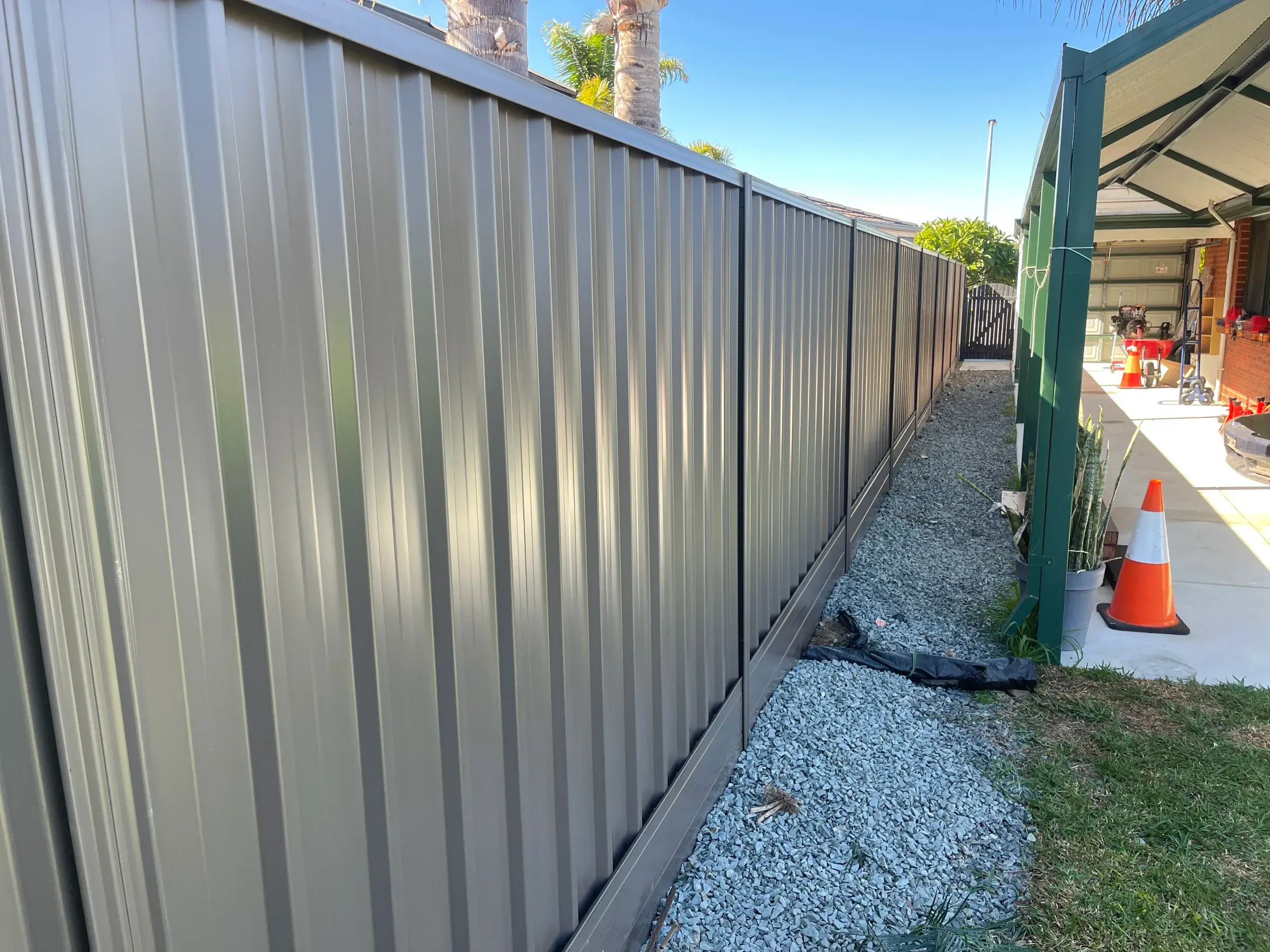 Grey Colorbond fence along a narrow side boundary with a gravel drainage strip at its base
