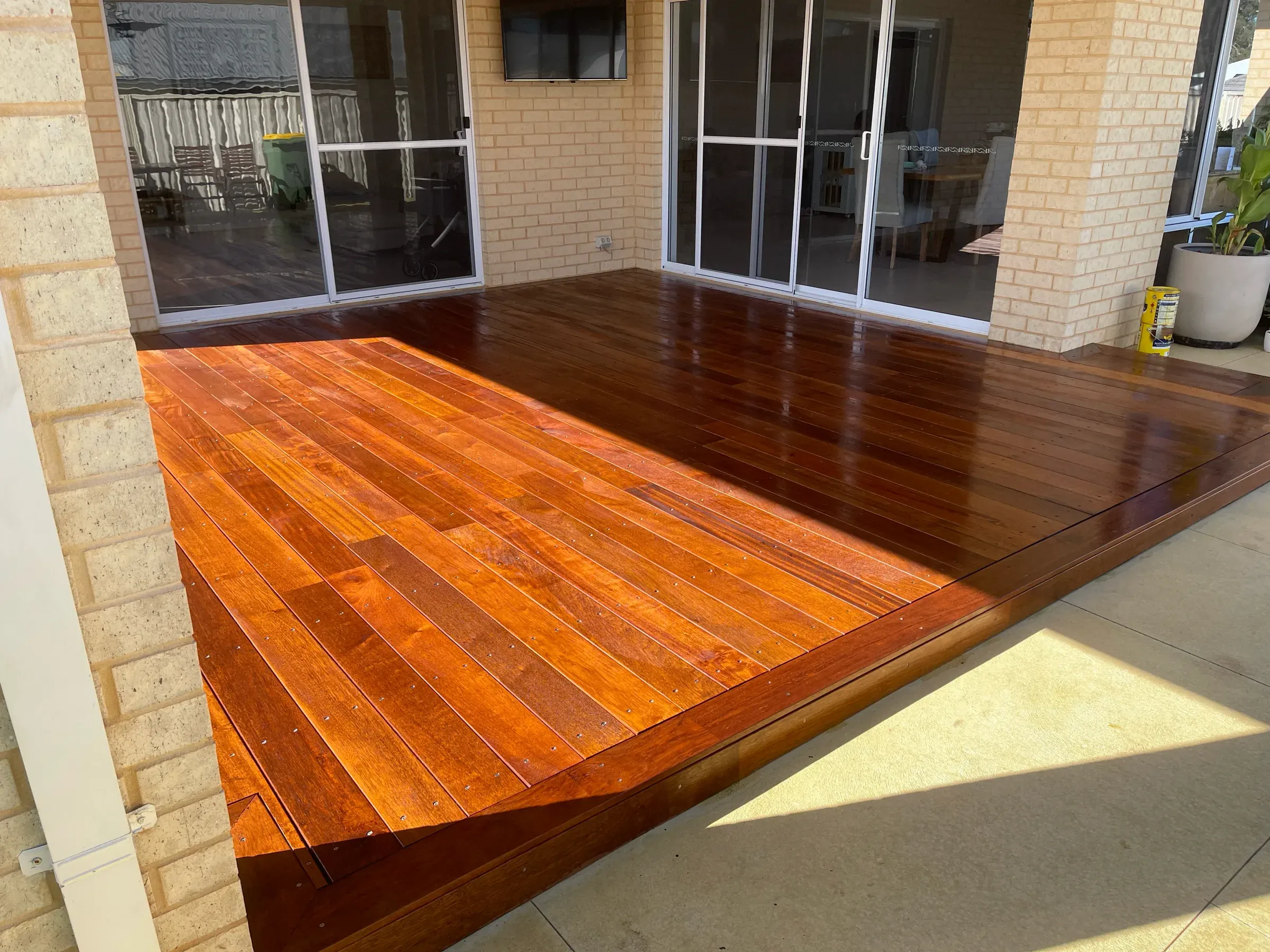 Freshly oiled jarrah deck boards catching the light outside sliding doors