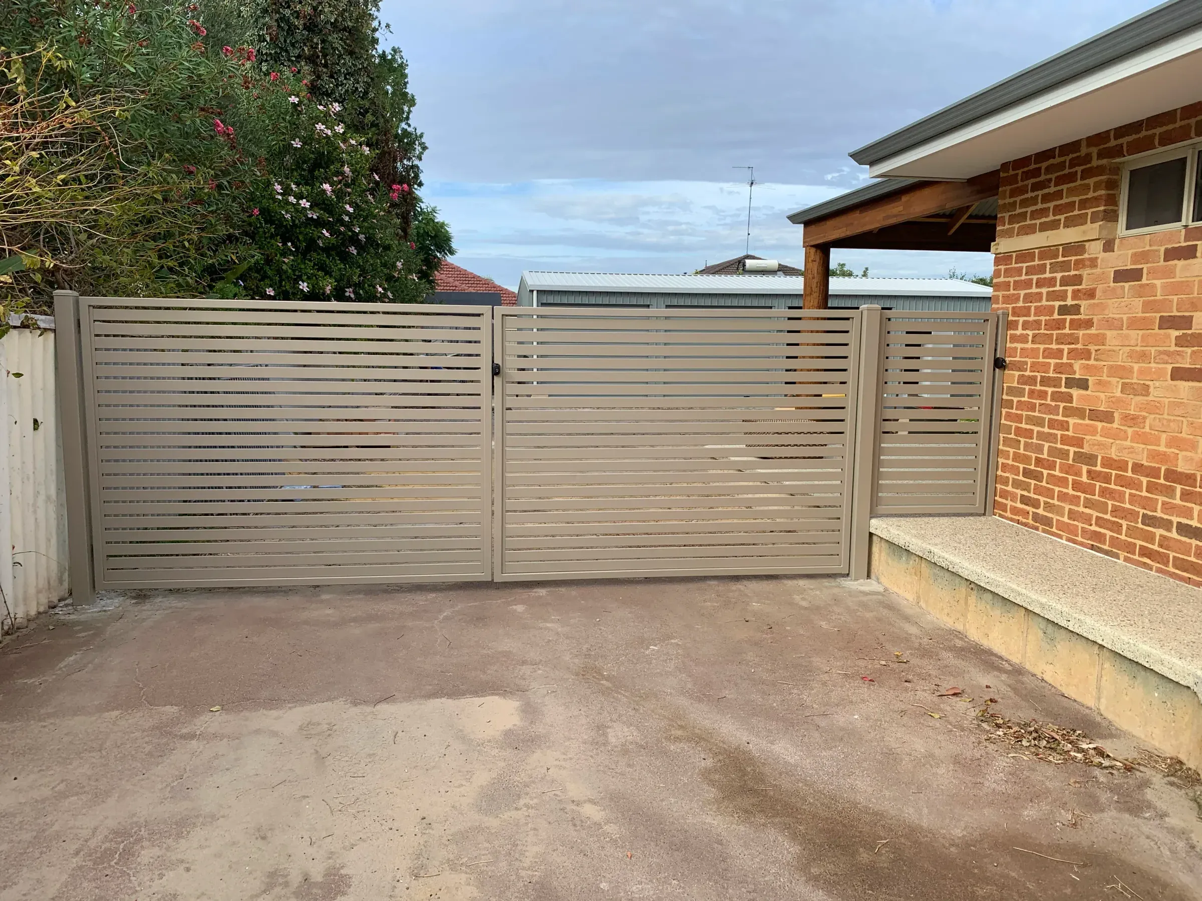Wide view of an aluminium slat double gate across a driveway with matching side panels