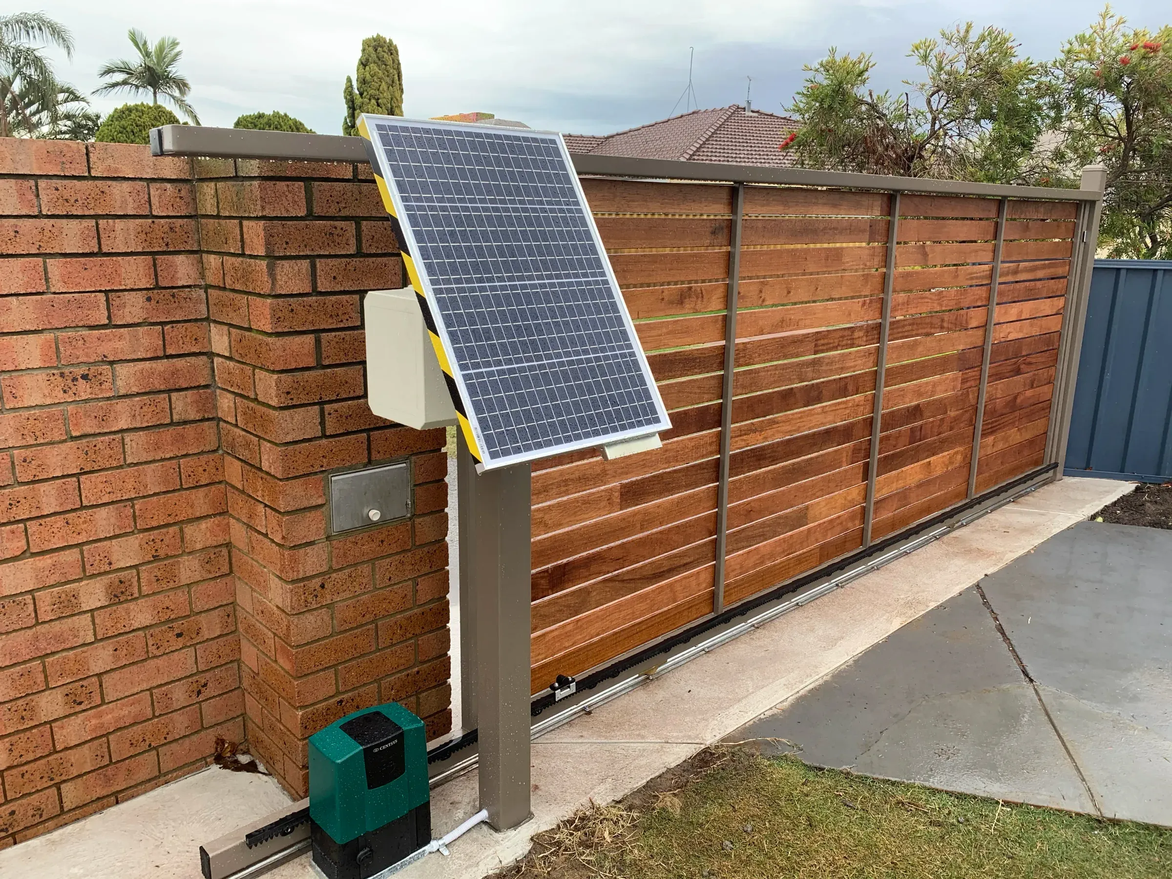 Solar panel and controller mounted on a brick pier beside an automated timber slat sliding gate
