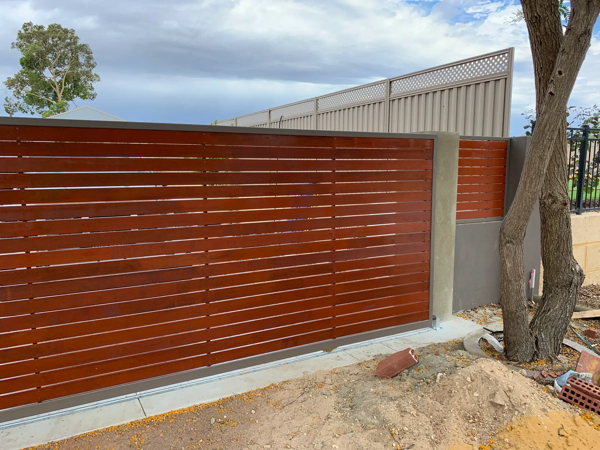 Merbau slat infill gate set into a Colorbond fence run beside a brick wall
