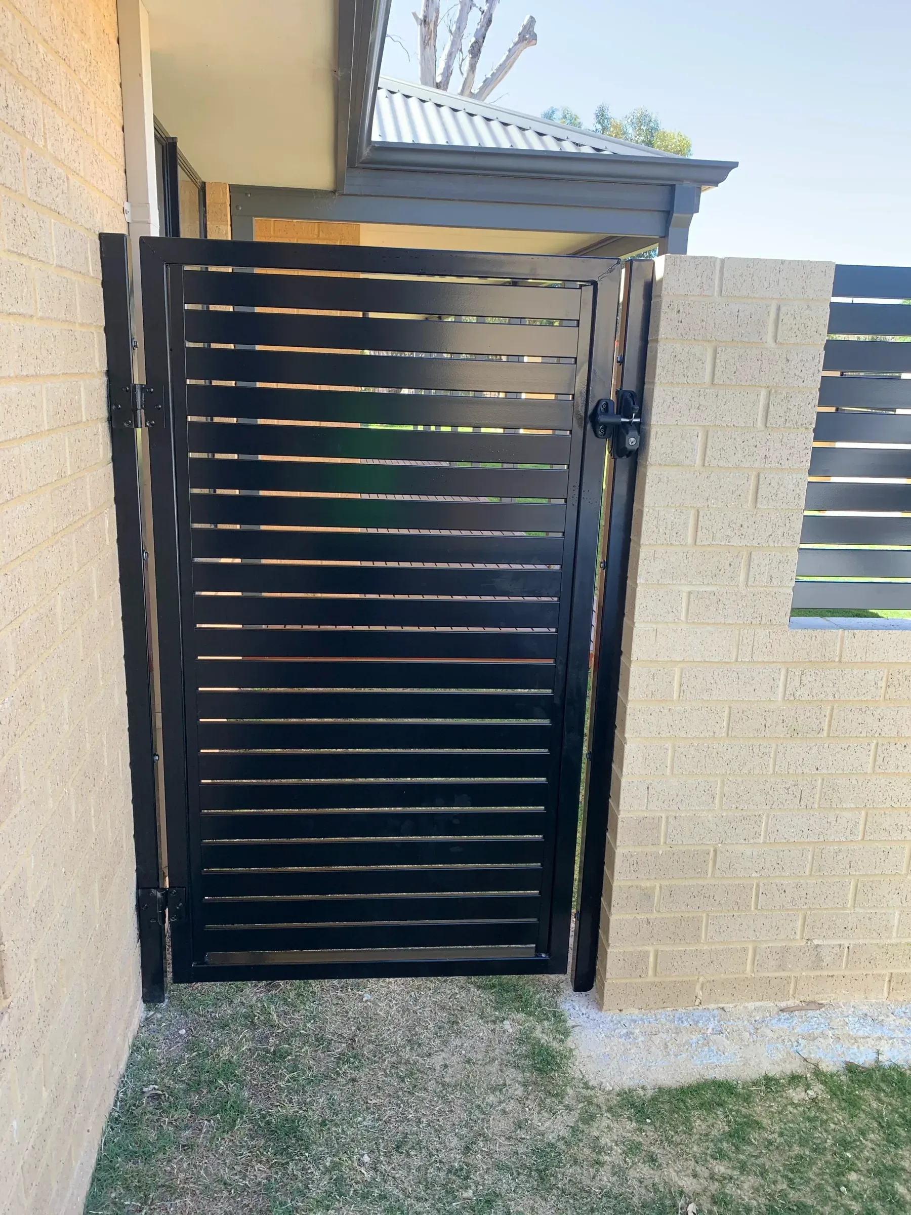 Black slat pedestrian gate set into a limestone block wall