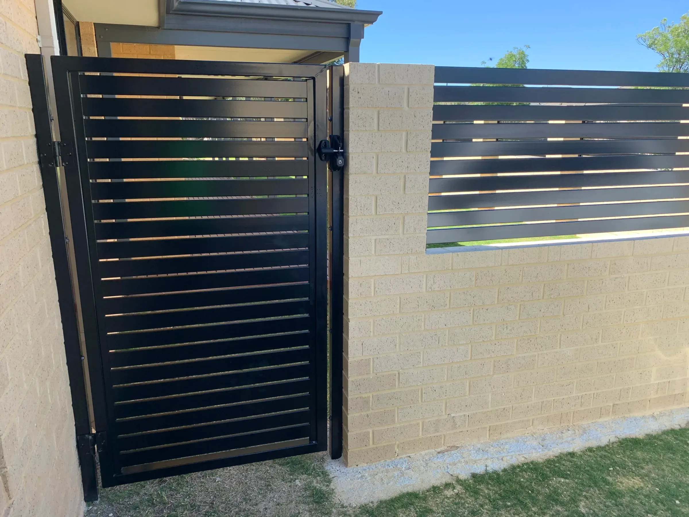 Black slat gate and slat-topped limestone wall seen from the street