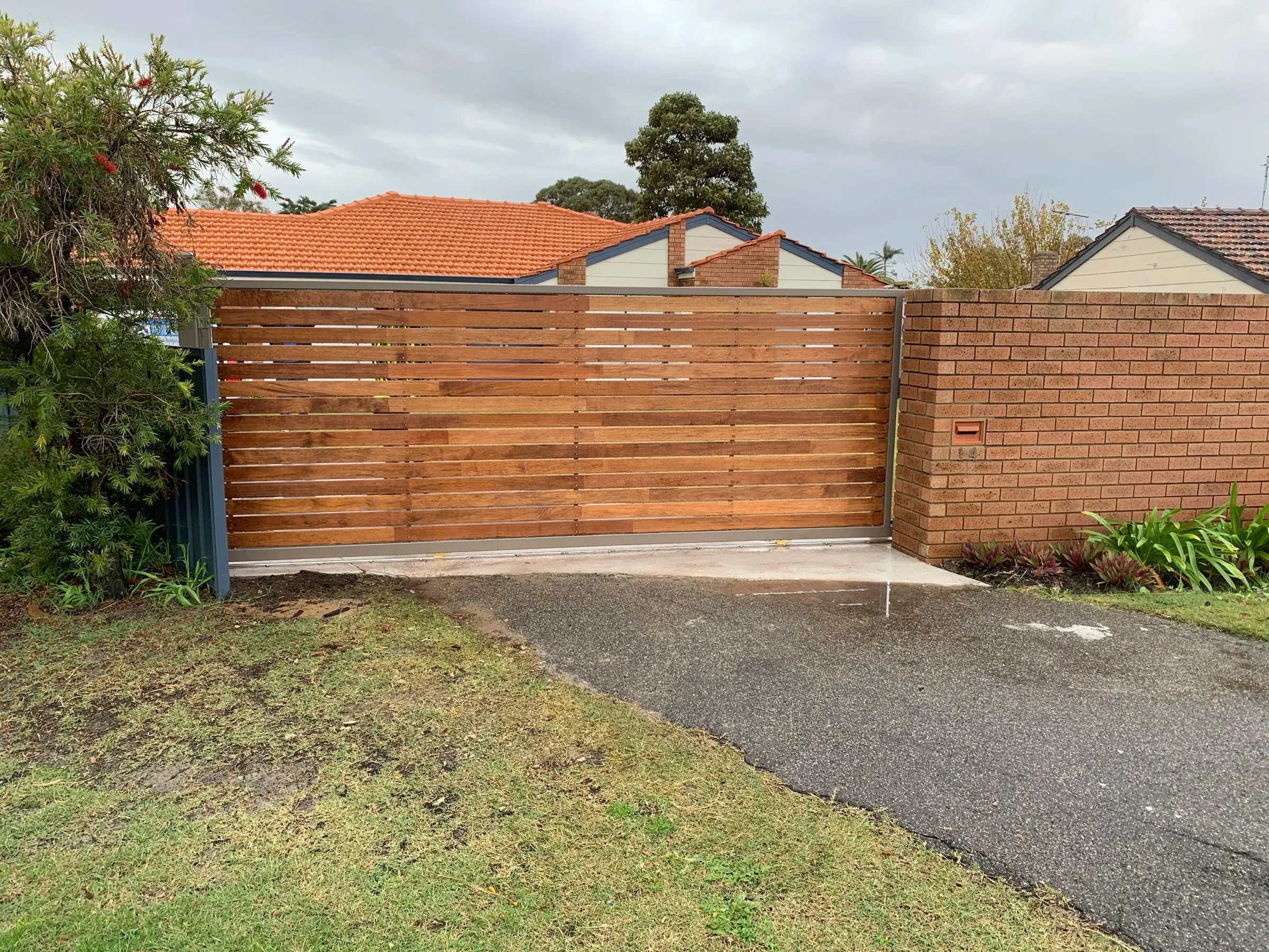 Timber slat double gate closed across a driveway between rendered piers