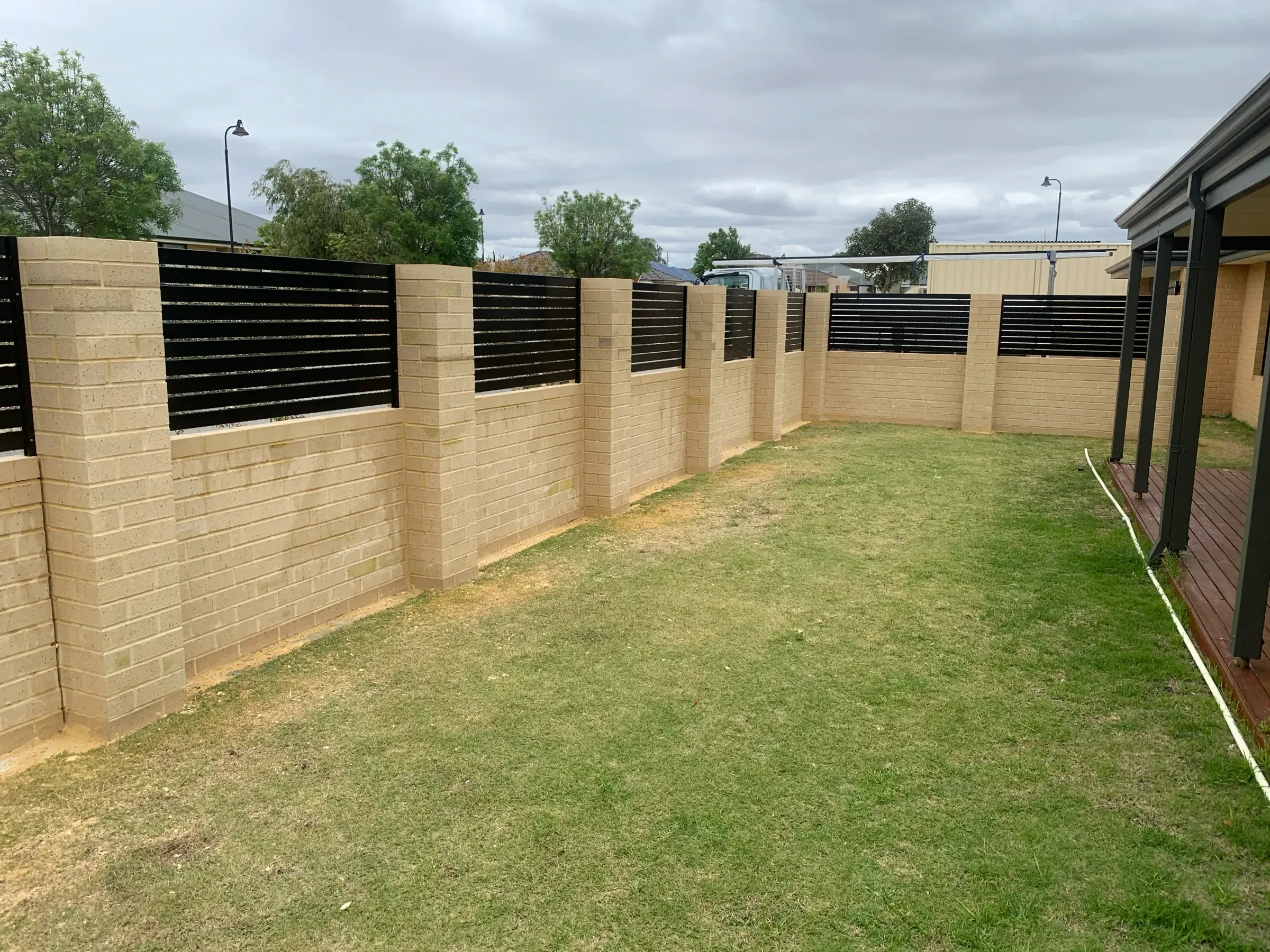 Limestone block wall and slat panels enclosing the rear boundary of a lawned yard