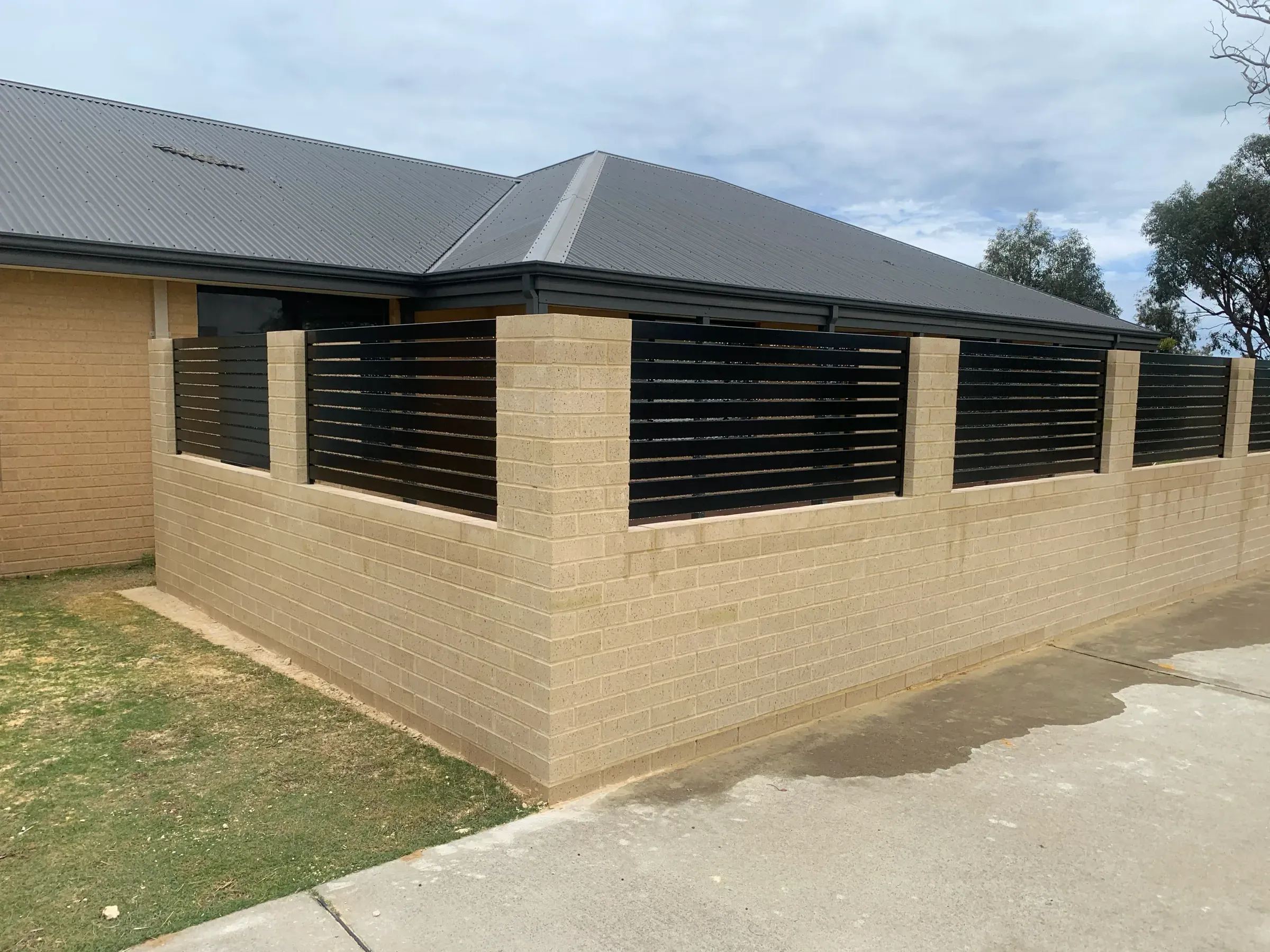 Limestone block wall topped with black aluminium slat panels around a corner block
