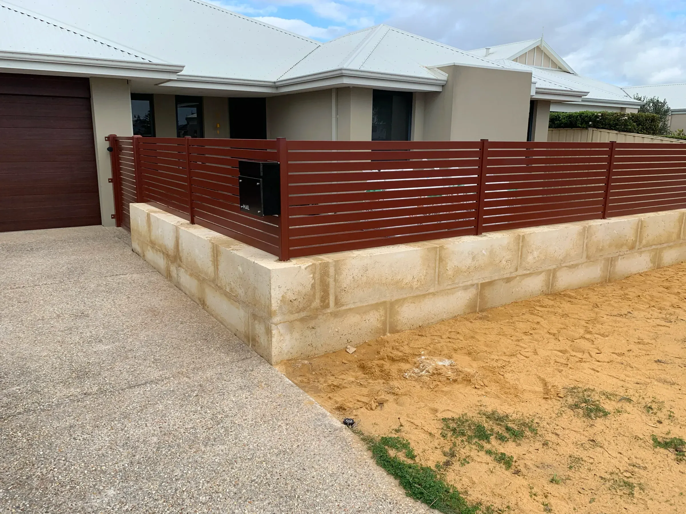 Low limestone retaining wall holding a raised front garden beside a concrete driveway