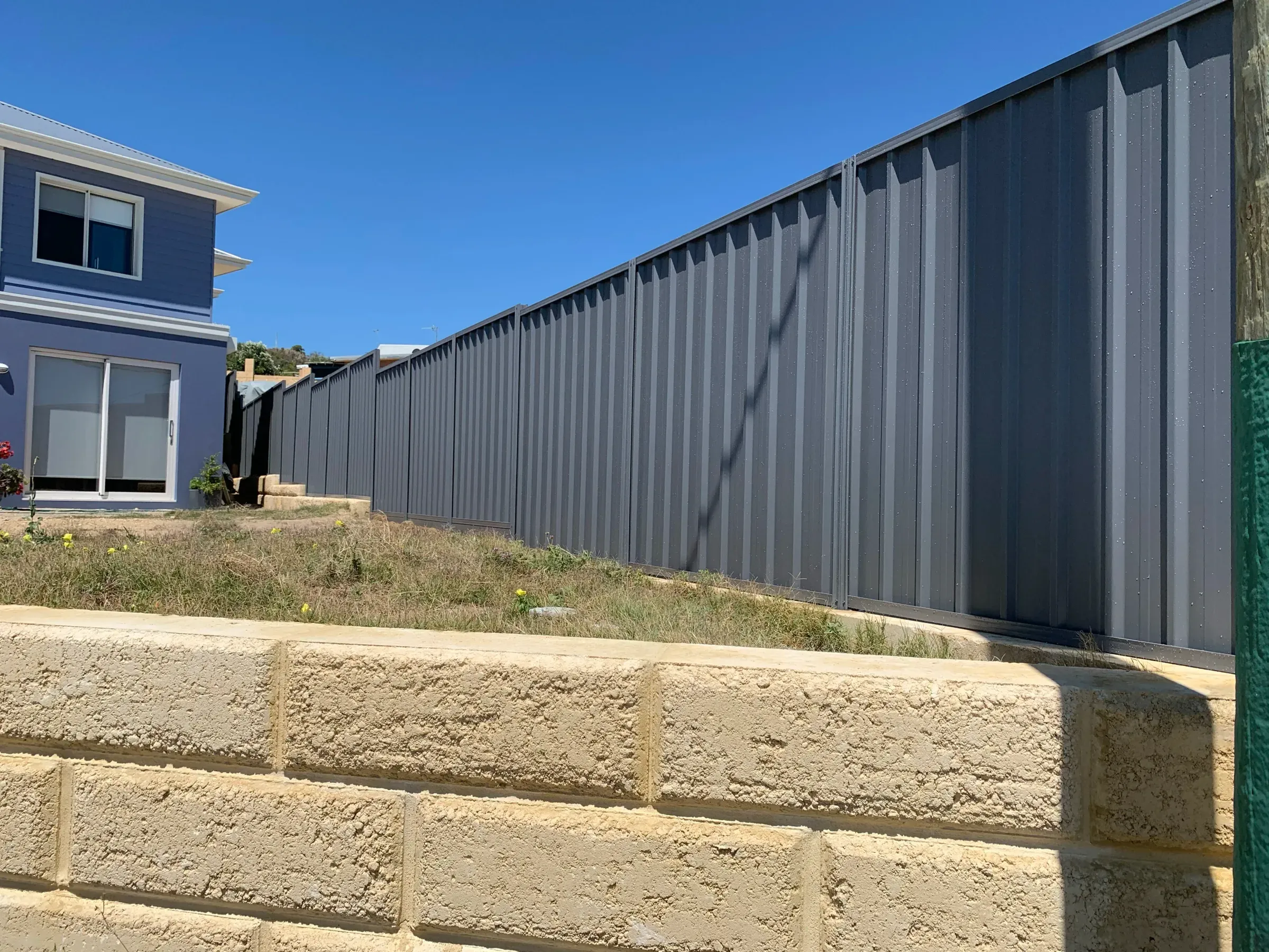 Limestone retaining wall with a Colorbond fence standing on the level above it