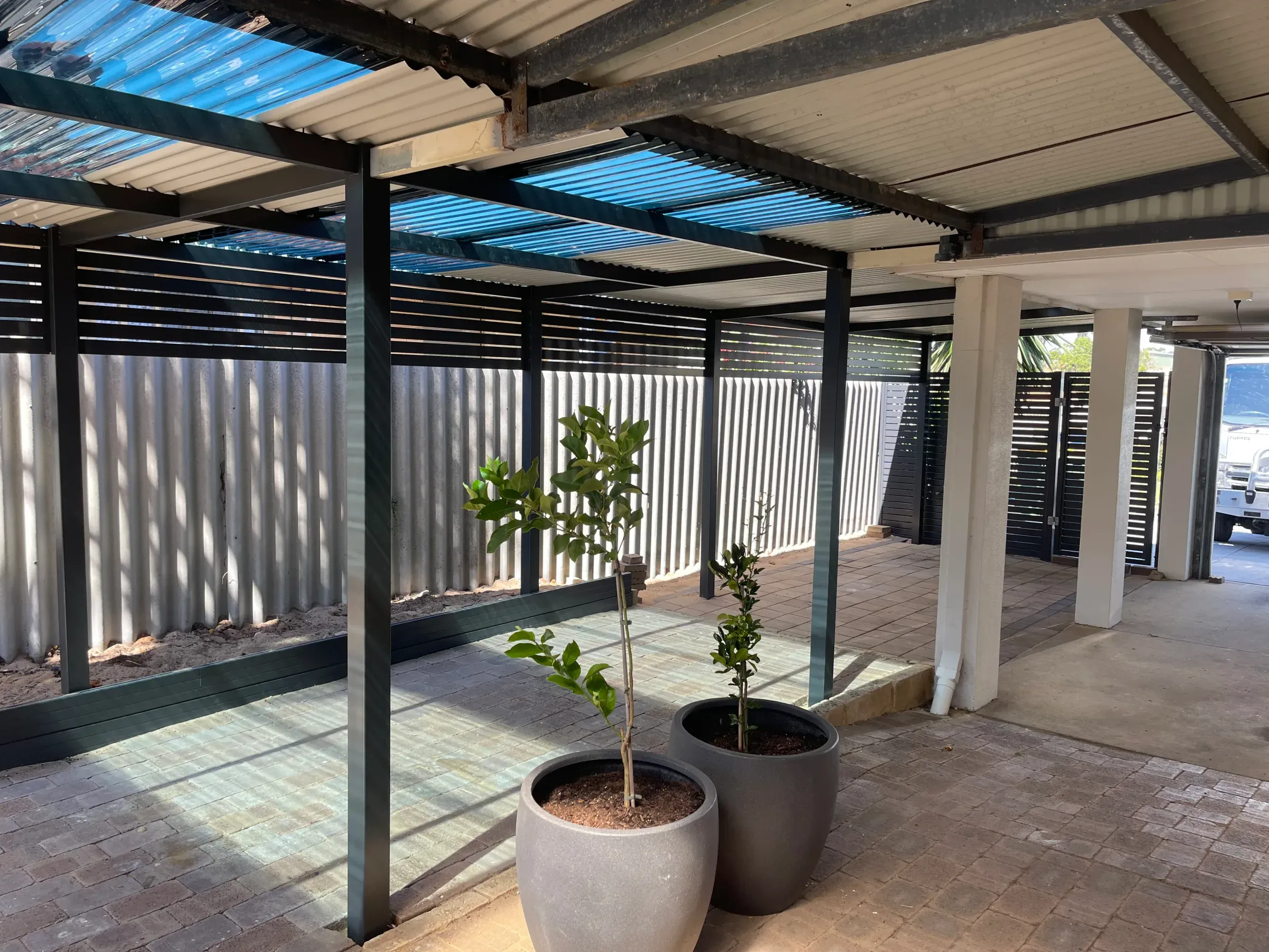 Flat-roof patio over a paved courtyard with potted trees and a slat screen