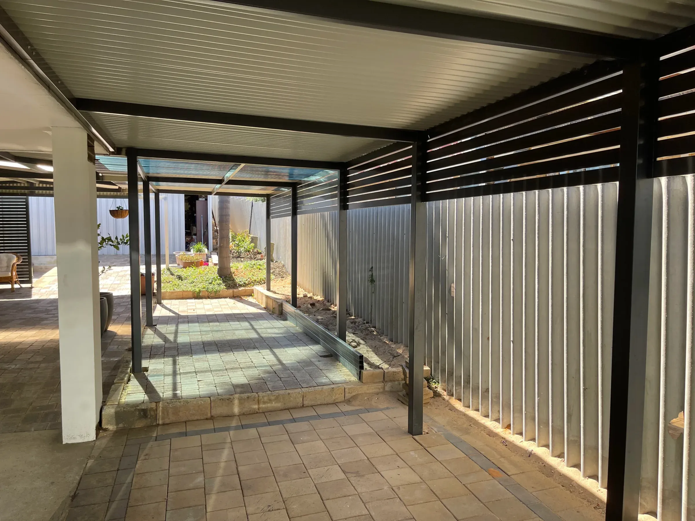 Flat-roof patio on posts over a brick paved courtyard beside a Colorbond fence