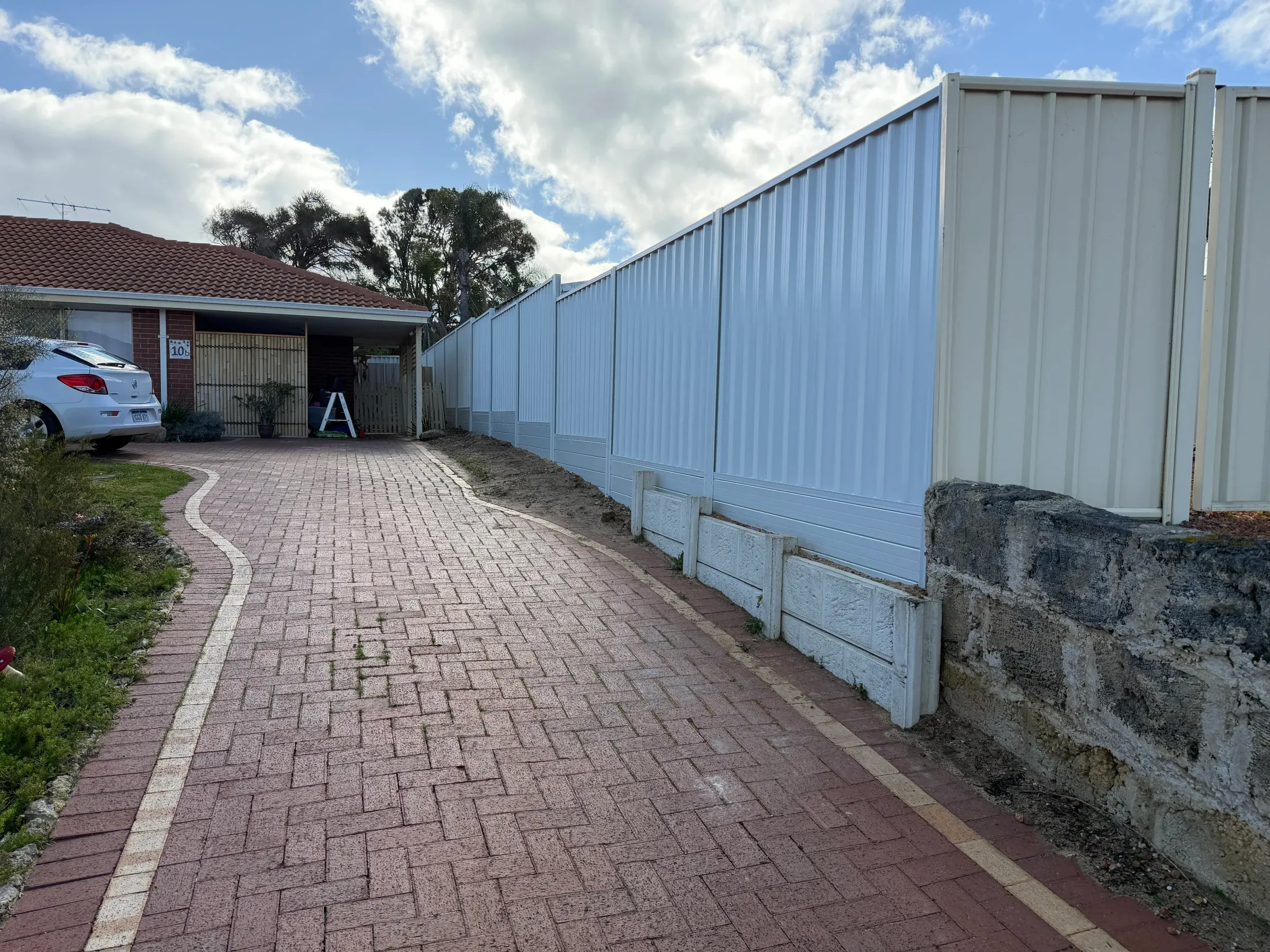 Brick paved driveway running down a side access past a limestone retaining wall