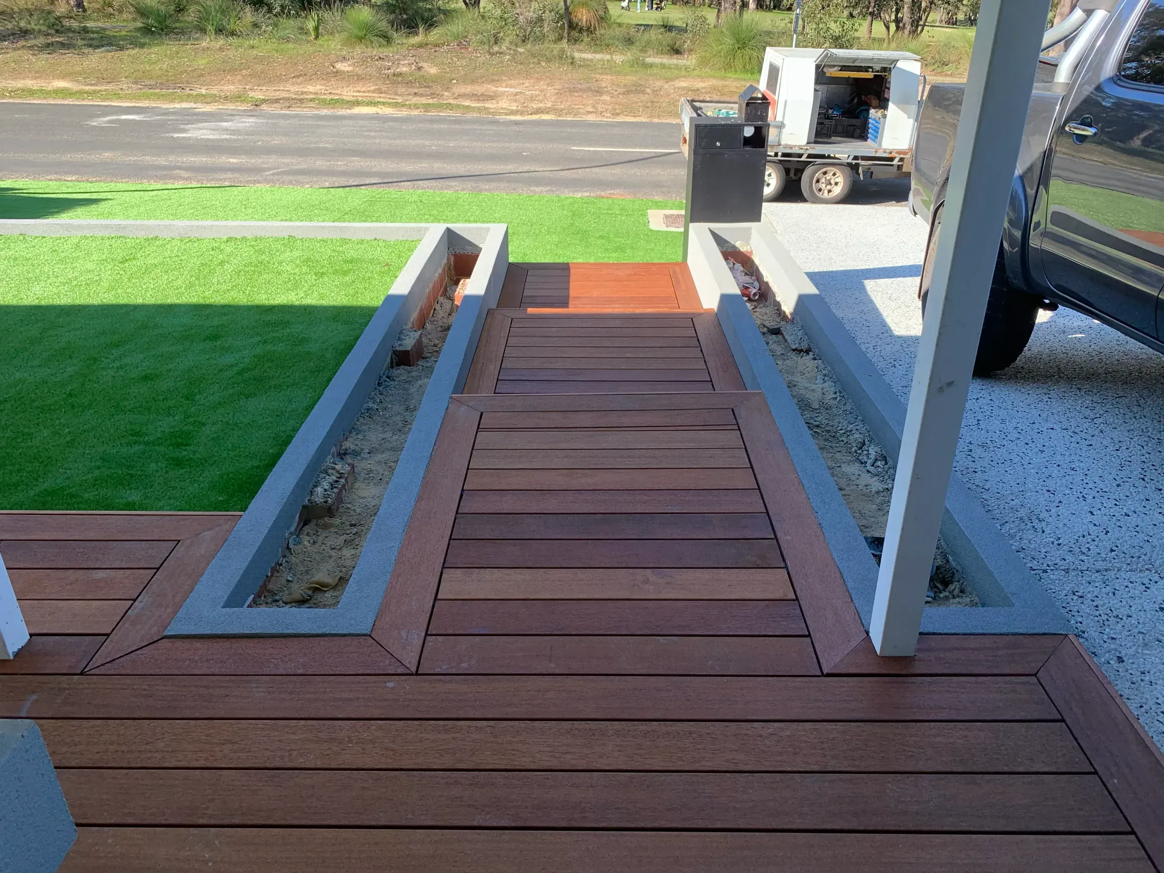 Paved path meeting a timber deck at a level threshold beside a garden bed