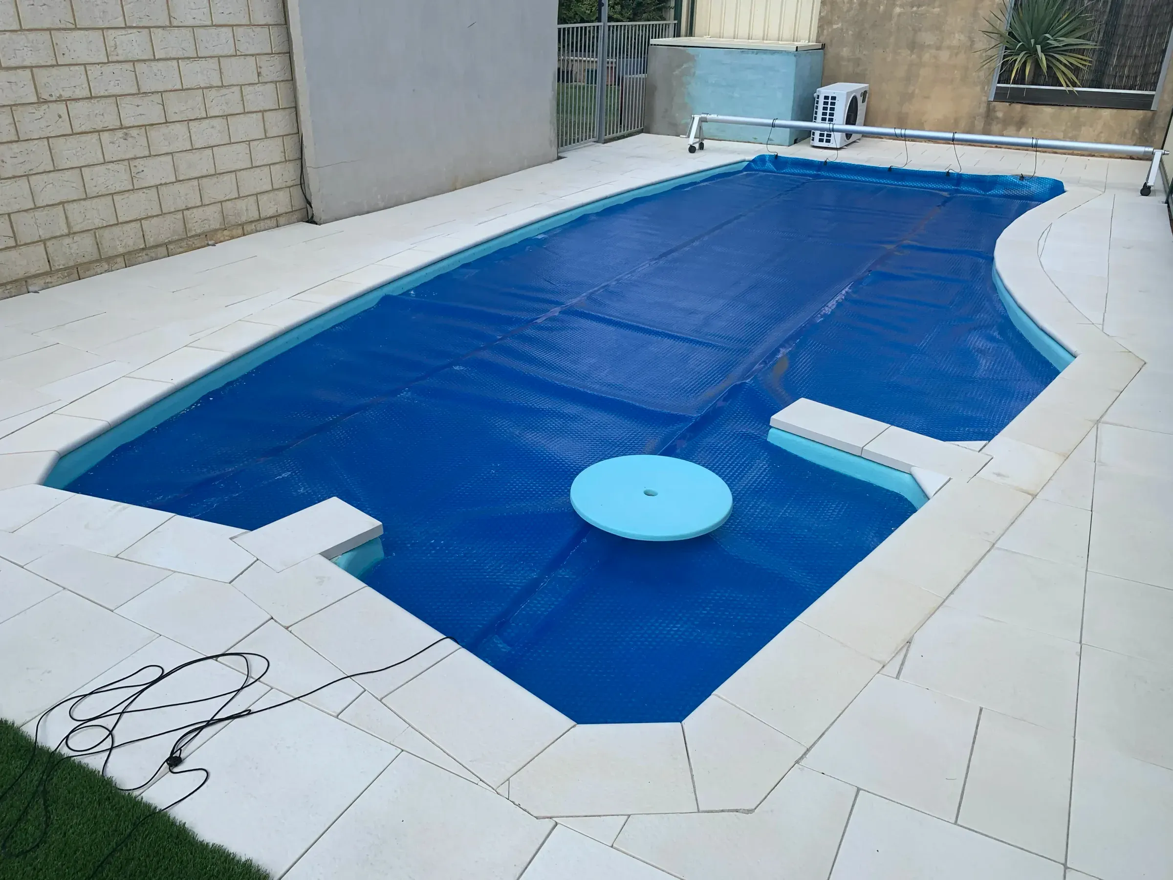 Wide view of a pale paved pool surround meeting the boundary fence and lawn