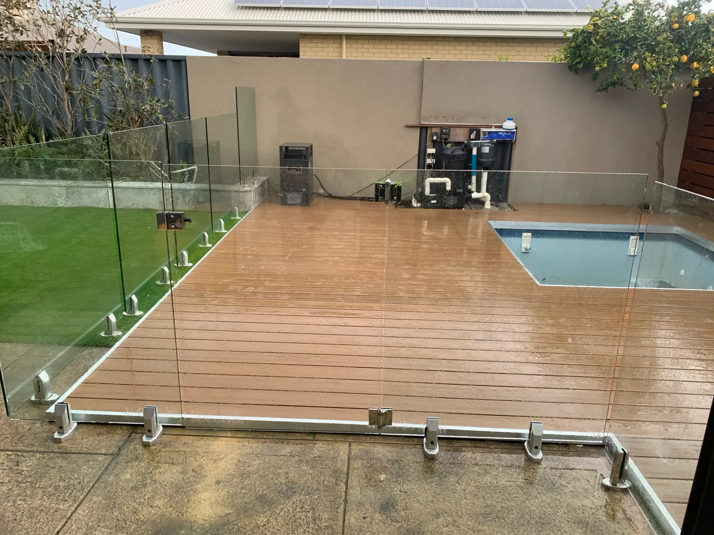Wide view of a glass pool barrier and timber deck against a slat boundary screen