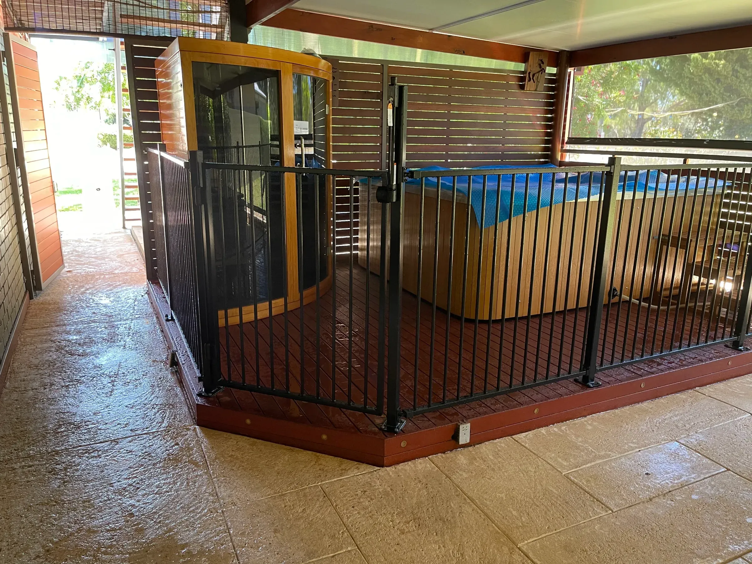 Black tubular pool fence and gate seen from under a patio roof