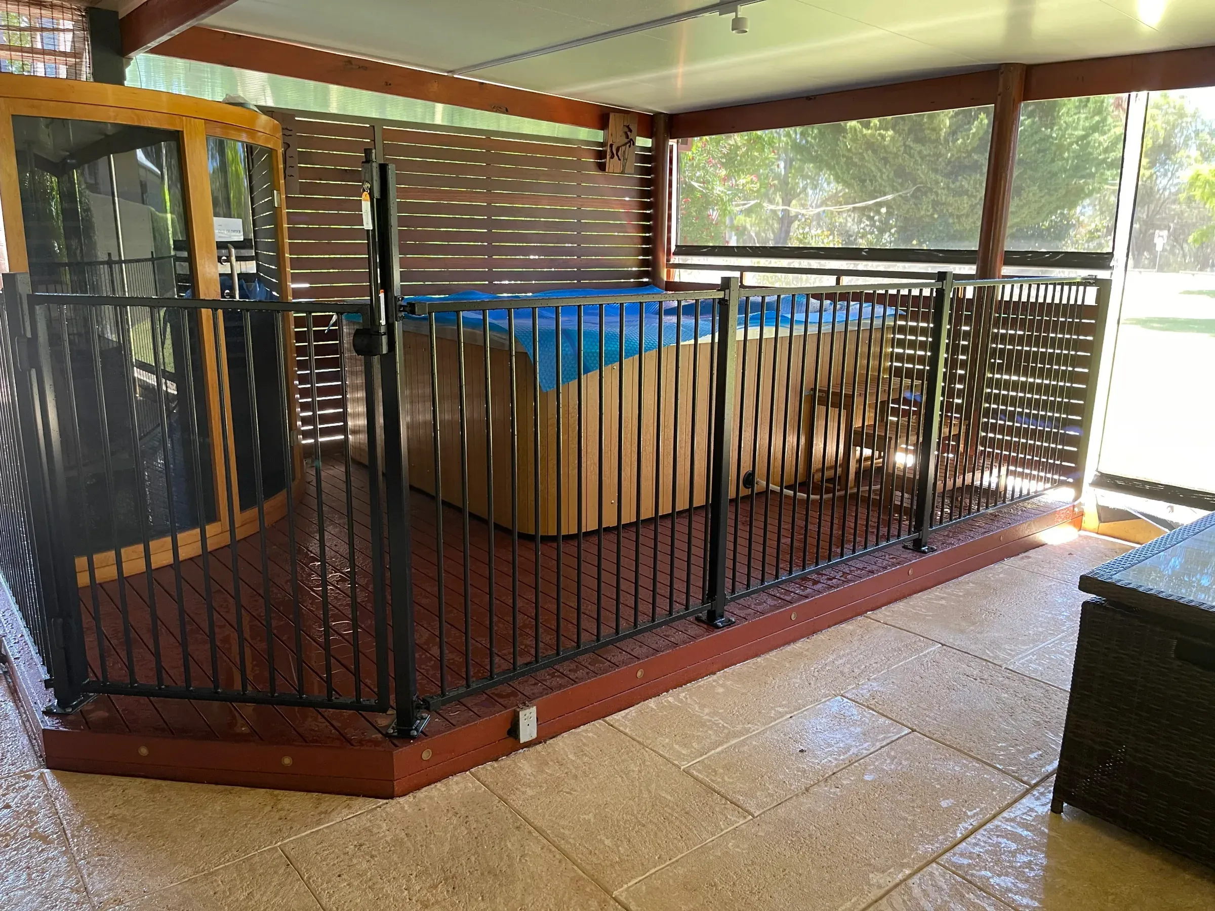 Black tubular pool fence enclosing a pool alongside a jarrah deck under a patio