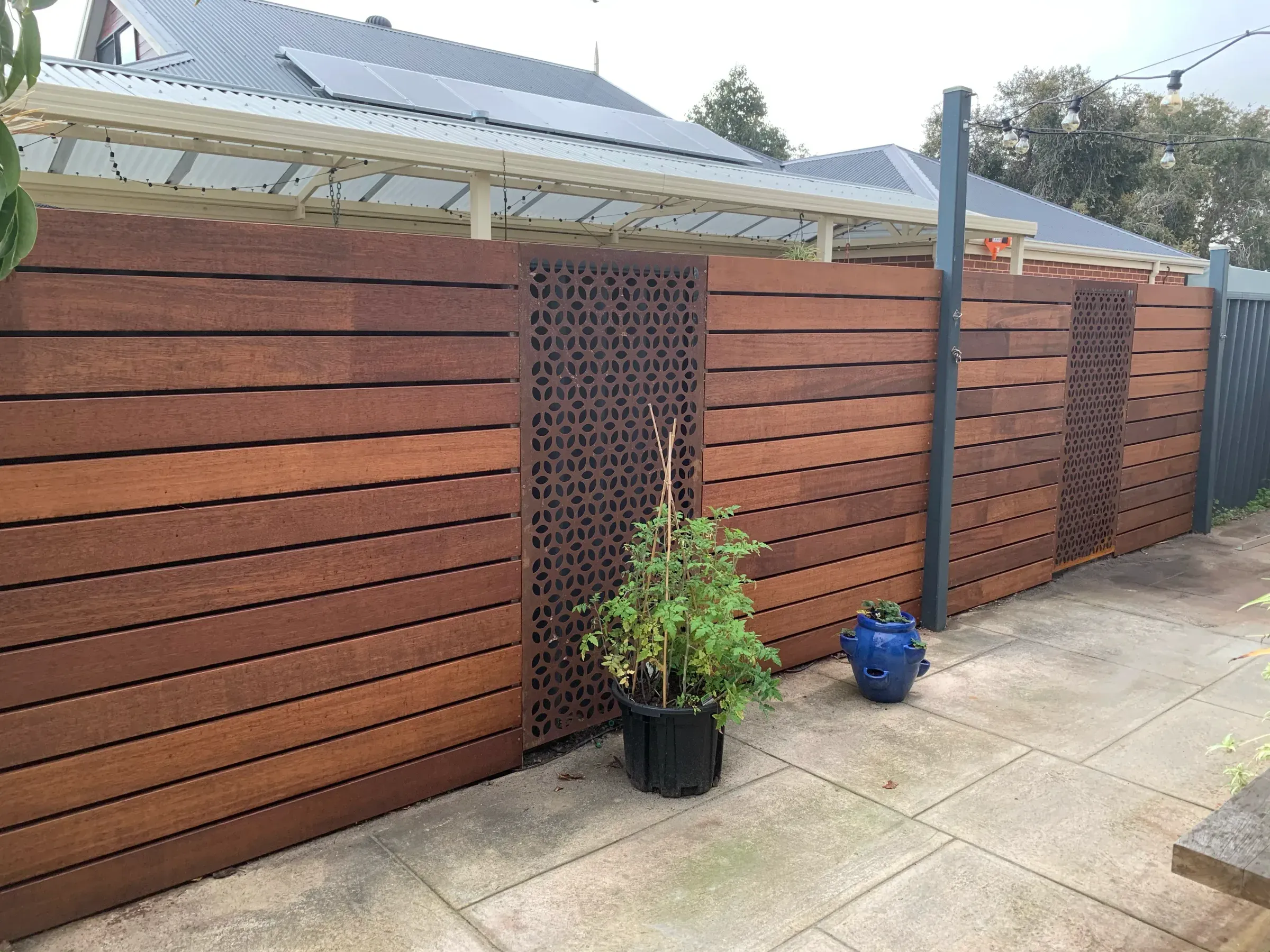 Merbau timber slat privacy screen with a decorative laser-cut panel beside a paved courtyard