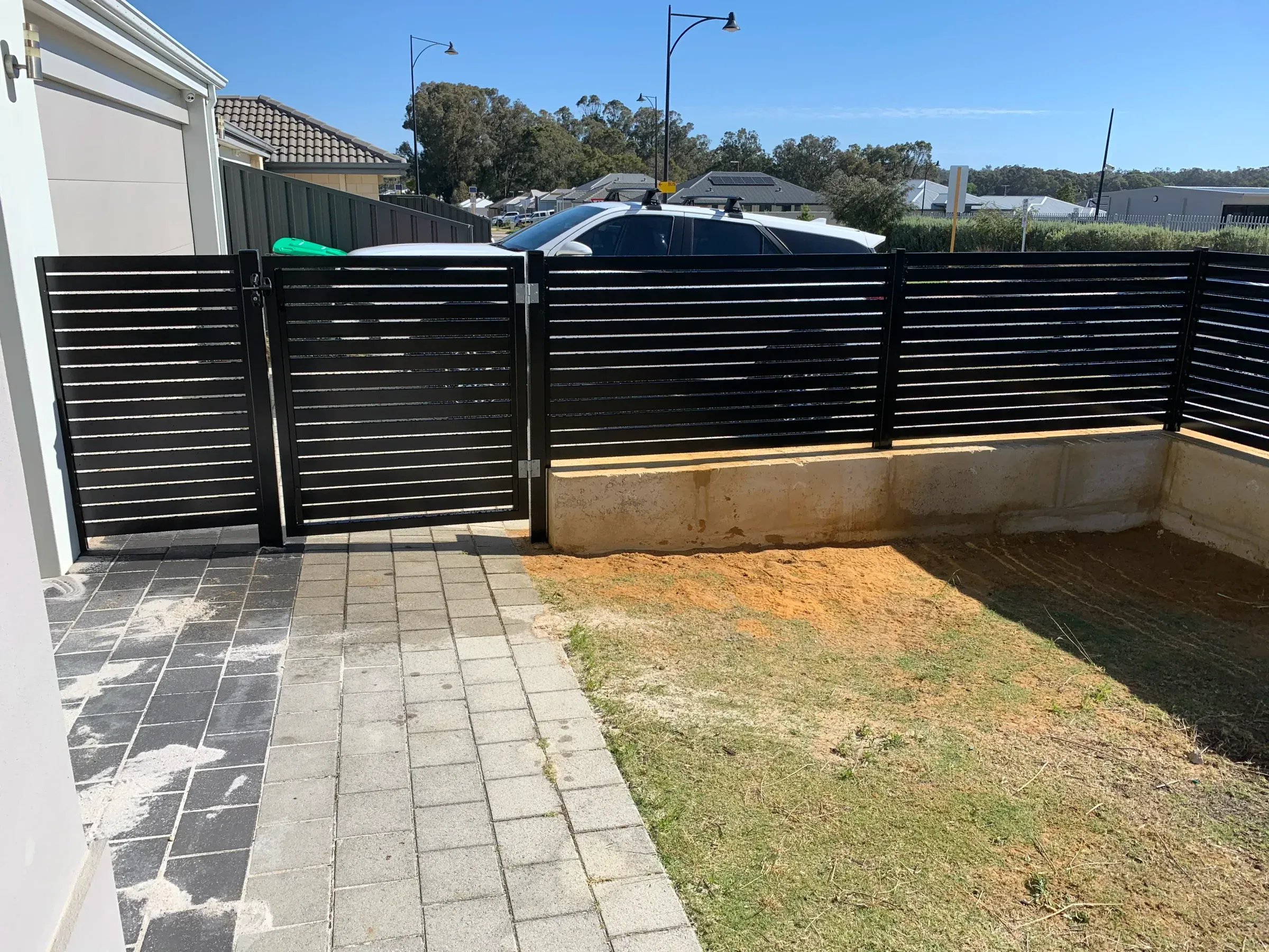 Black aluminium slat double gate closed across a paved driveway with matching fence panels