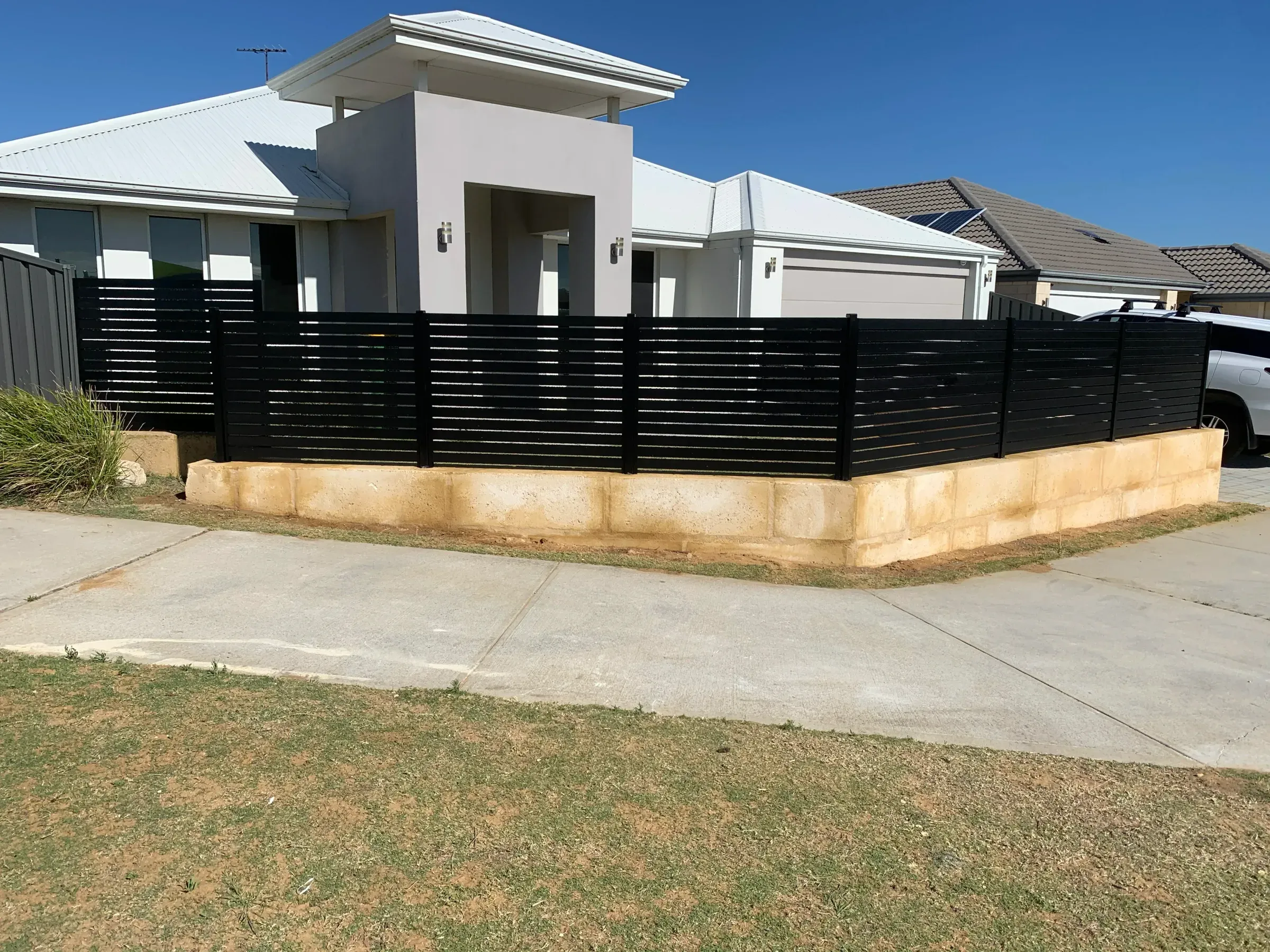Black aluminium slat fence turning the corner of a limestone base onto a paved driveway