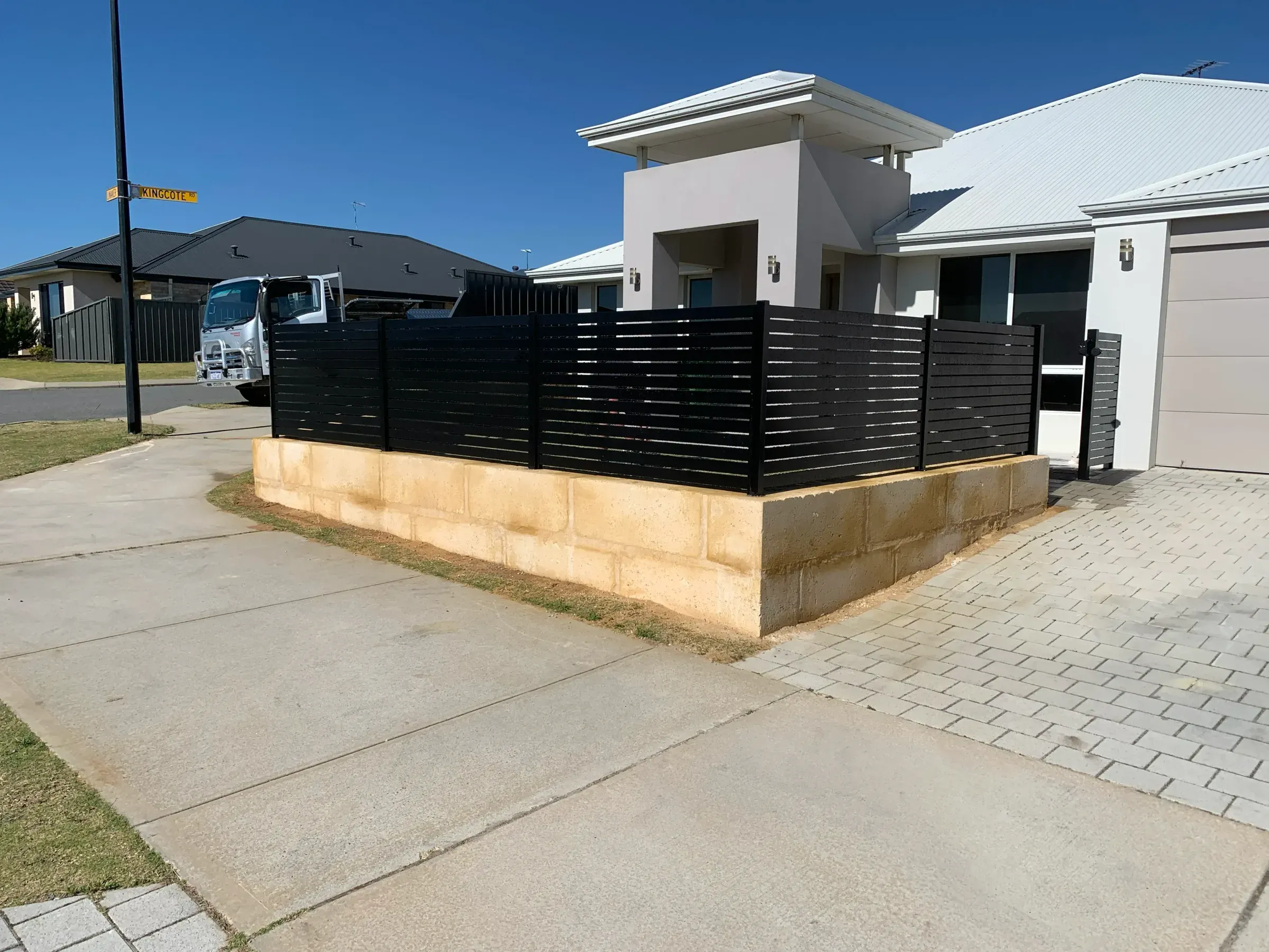 Black aluminium slat fence following the curve of a limestone garden wall