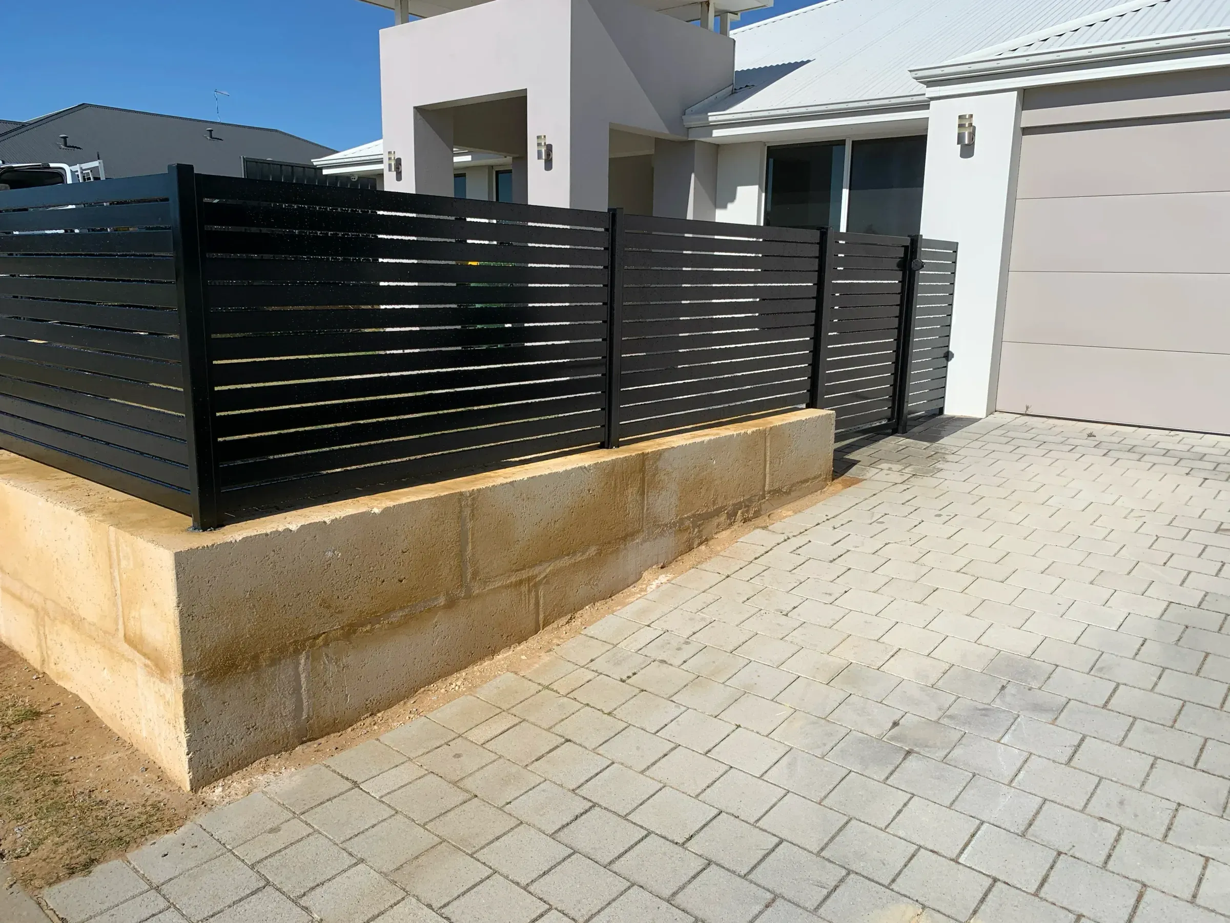 Black aluminium slat fence set on a limestone block base across the frontage of a new house