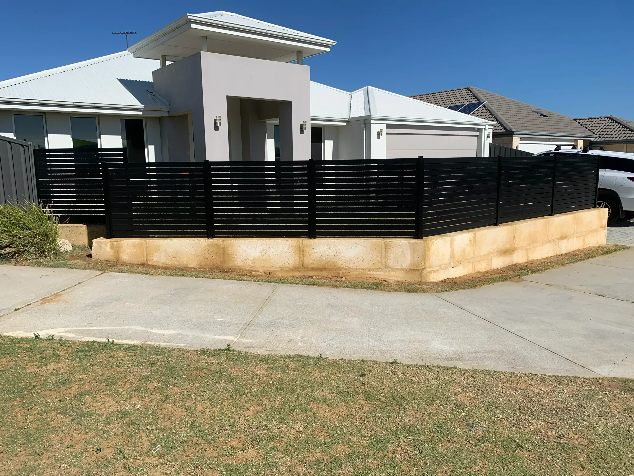 Black aluminium slat fencing and limestone walling running the length of a new streetscape