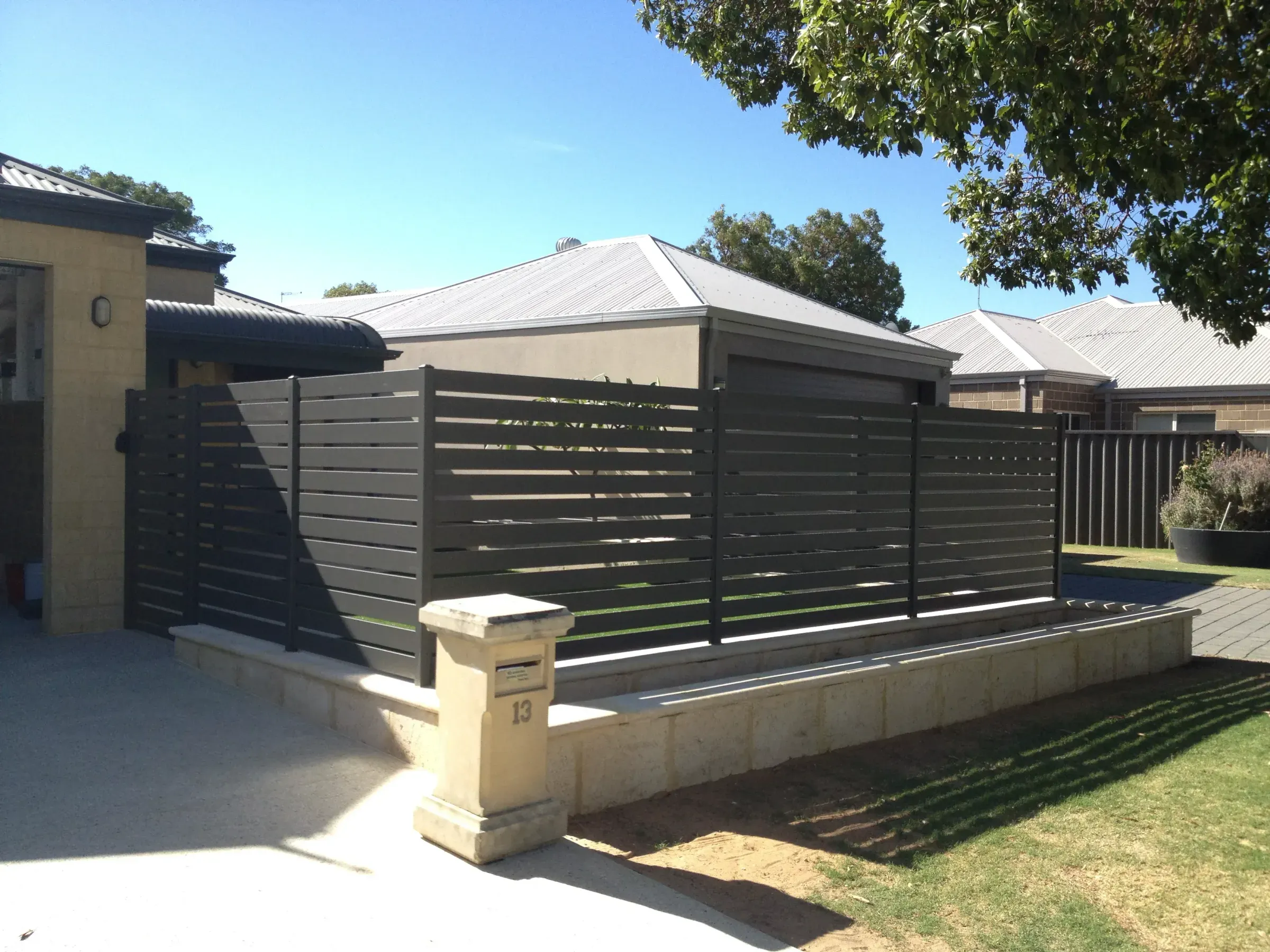 Charcoal slat fence and limestone piers running beside a driveway to the street
