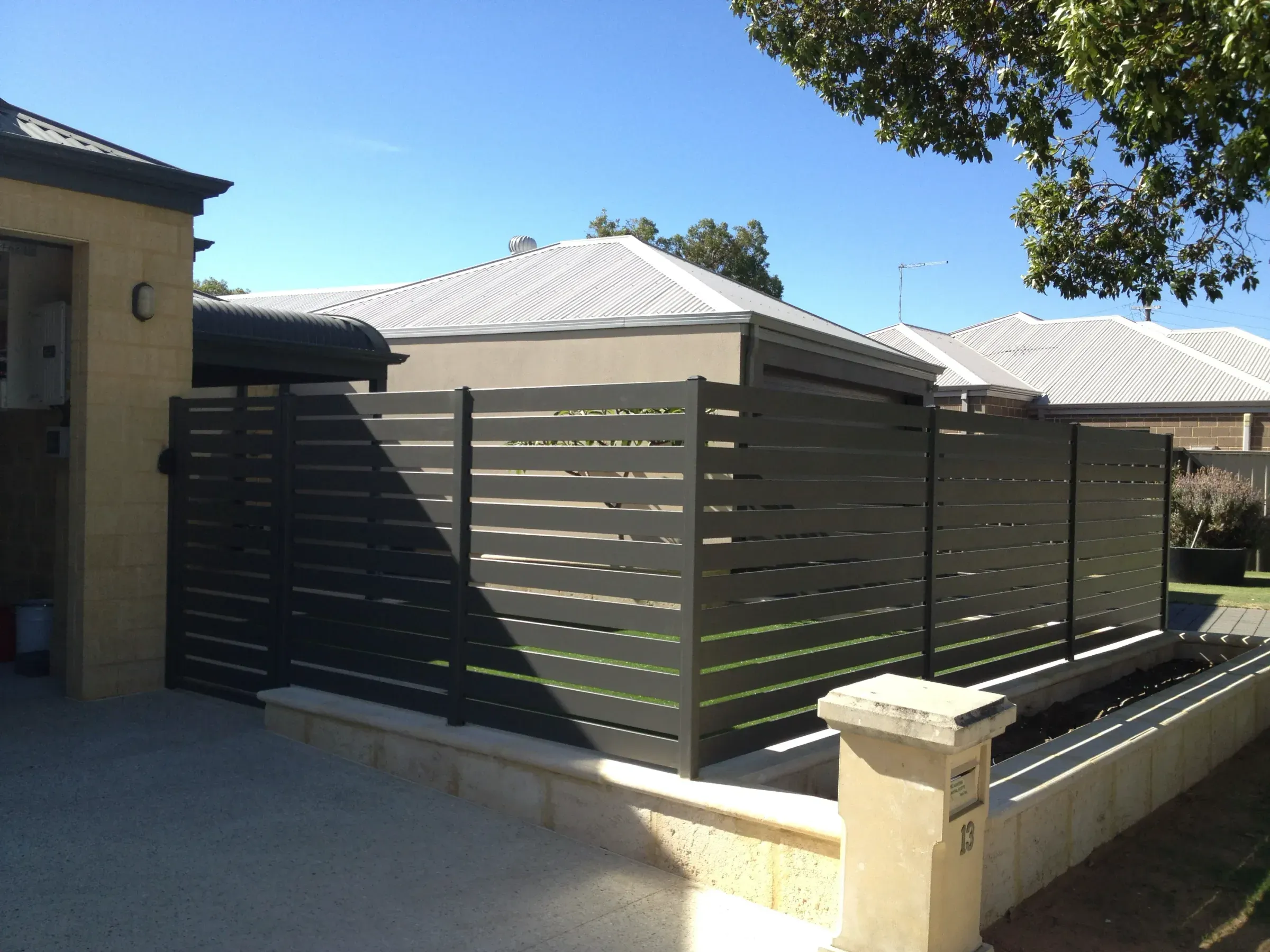 Charcoal aluminium slat panels set between limestone piers on a front boundary
