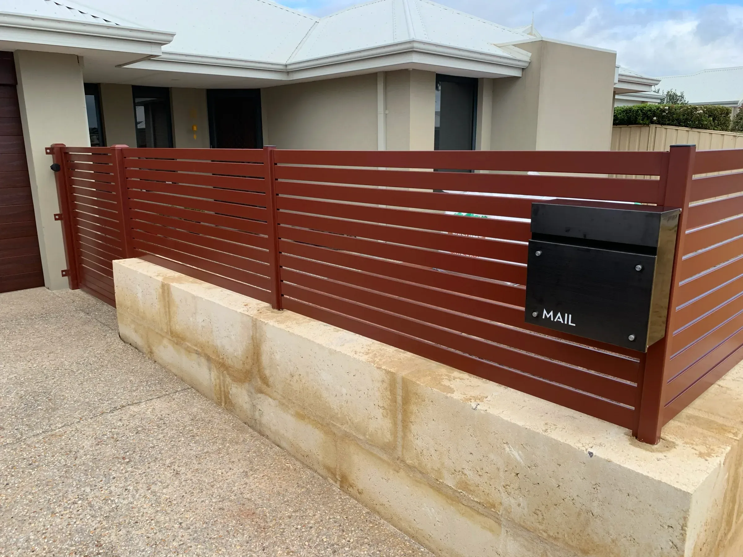 Merbau-stained slat fence on a limestone retaining base across a house frontage
