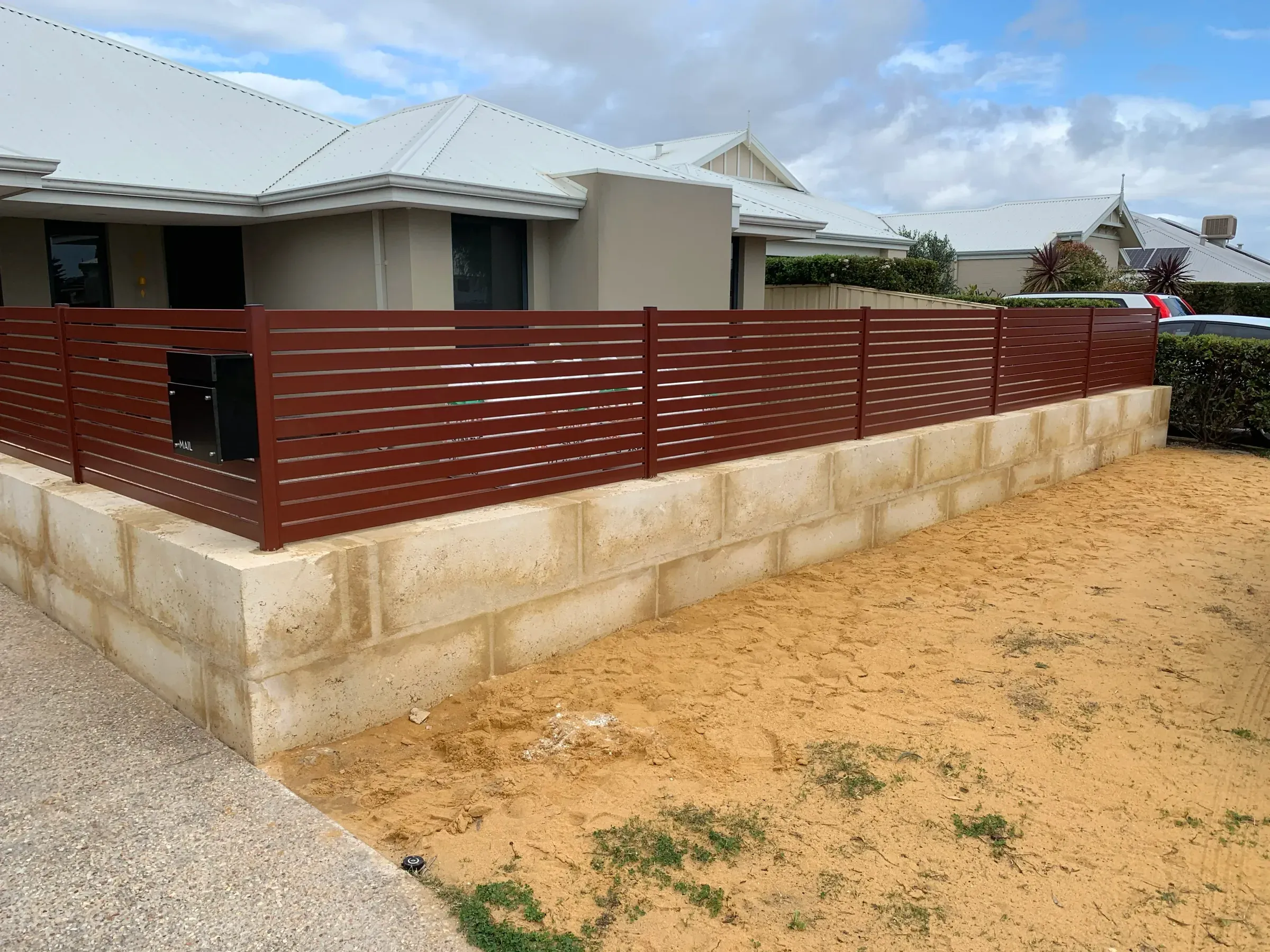 Wide view of a stained slat fence and limestone base running to the driveway crossover