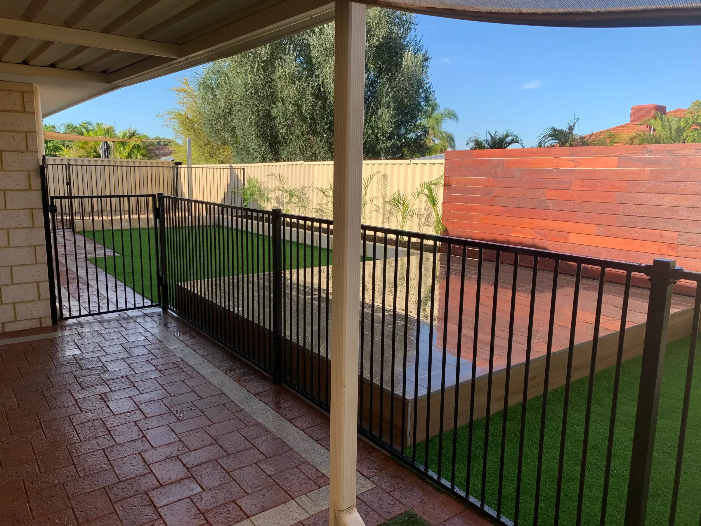Black tubular pool fence running across a backyard, with a cream Colorbond boundary fence behind it